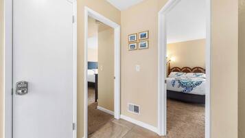 A hotel room with a bed, a bedside table, a lamp, and a door with a keypad lock.