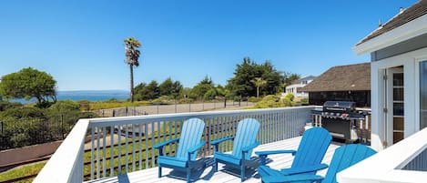 A deck with blue Adirondack chairs and a grill, overlooking a scenic view.