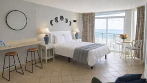 Une chambre d’hôtel avec un lit, deux tables de chevet, une chaise, une petite table et une vue sur la mer.