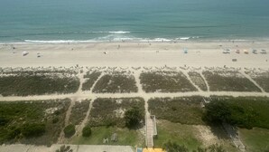 Une plage offrant une vue dégagée sur l’océan, avec du sable fin et une promenade en bois menant à l’eau.
