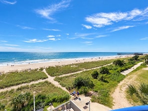 A beach with a pier, clear skies, and a path leading to a building.