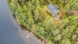 An aerial view of a cabin surrounded by dense forest, with a dock extending into a lake.