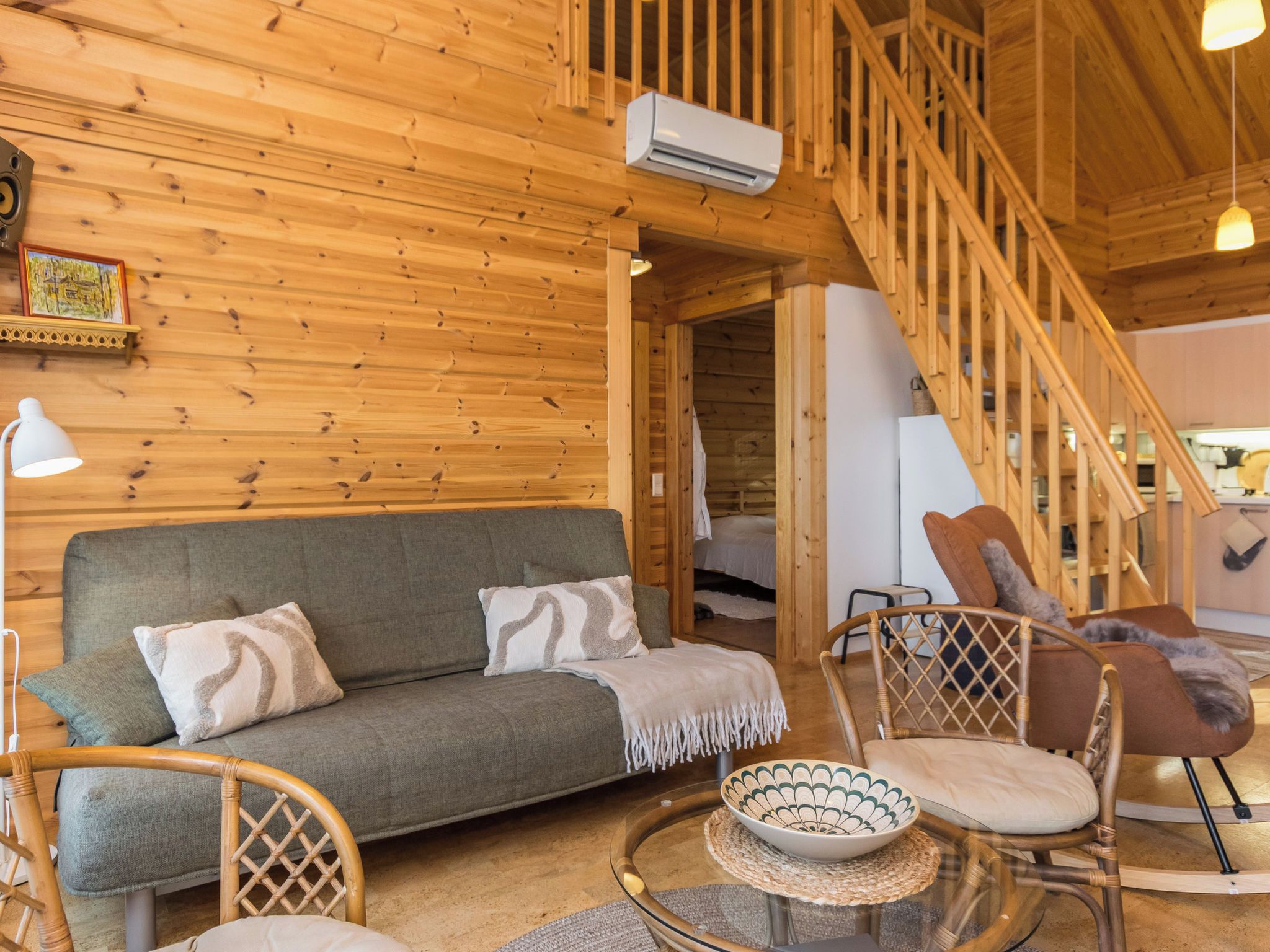 Een houten interieur met een bank, stoelen, een trap en een airconditioning.