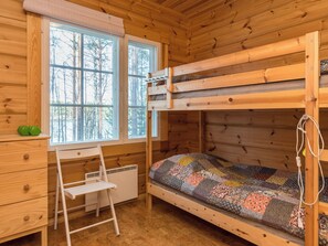 A bunk bed with a quilt, a desk with drawers, a chair, and a radiator.