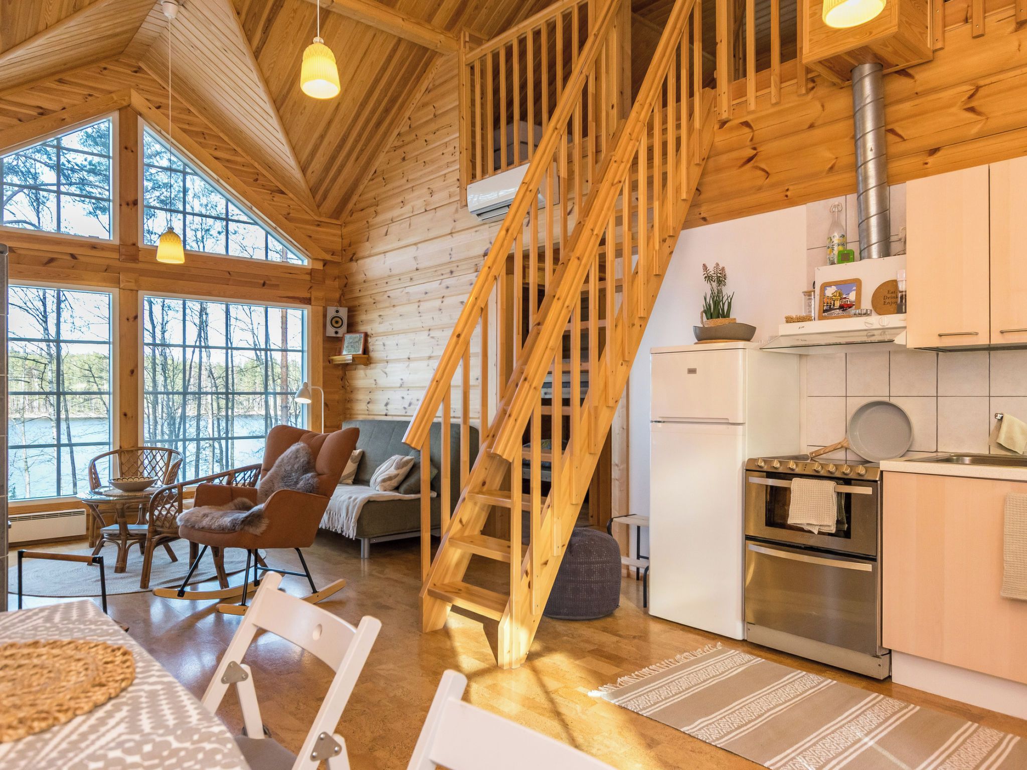 Een houten interieur met een trap, keuken, eethoek en grote ramen.