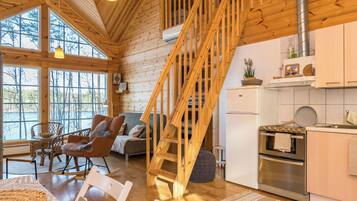 Een houten interieur met een trap, keuken, eethoek en grote ramen.