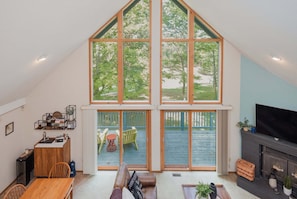 A loft-style room with a high ceiling, large windows, a fireplace, and a dining area. - Fireplace, Fire Pit, Covered Porch & Resort Access (Hedgesville)