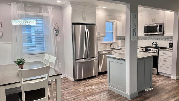 A modern kitchen with white cabinetry, stainless steel appliances, and a wooden floor.