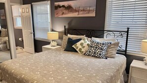 A bedroom with a bed, nightstands, a lamp, a painting, and a door.