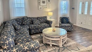 A living room with a sectional sofa, a round glass coffee table, a chair, and a ceiling fan.