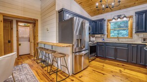 A kitchen with wooden floors, a stainless steel refrigerator, a built-in oven, and a window with a view of trees. - Dome, Hammock, Sauna, Golf, Best Location in BR (Blue Ridge)