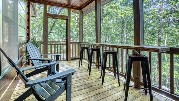 A wooden deck with a table and chairs, large windows, and a view of the forest. - Dome, Hammock, Sauna, Golf, Best Location in BR (Blue Ridge)