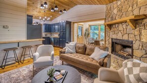 A cozy cabin interior with a stone fireplace, wooden ceiling, and a dining area with bar stools. - Dome, Hammock, Sauna, Golf, Best Location in BR (Blue Ridge)