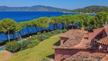 A coastal villa with terracotta roofs, a swimming pool, and a view of the sea and distant hills.