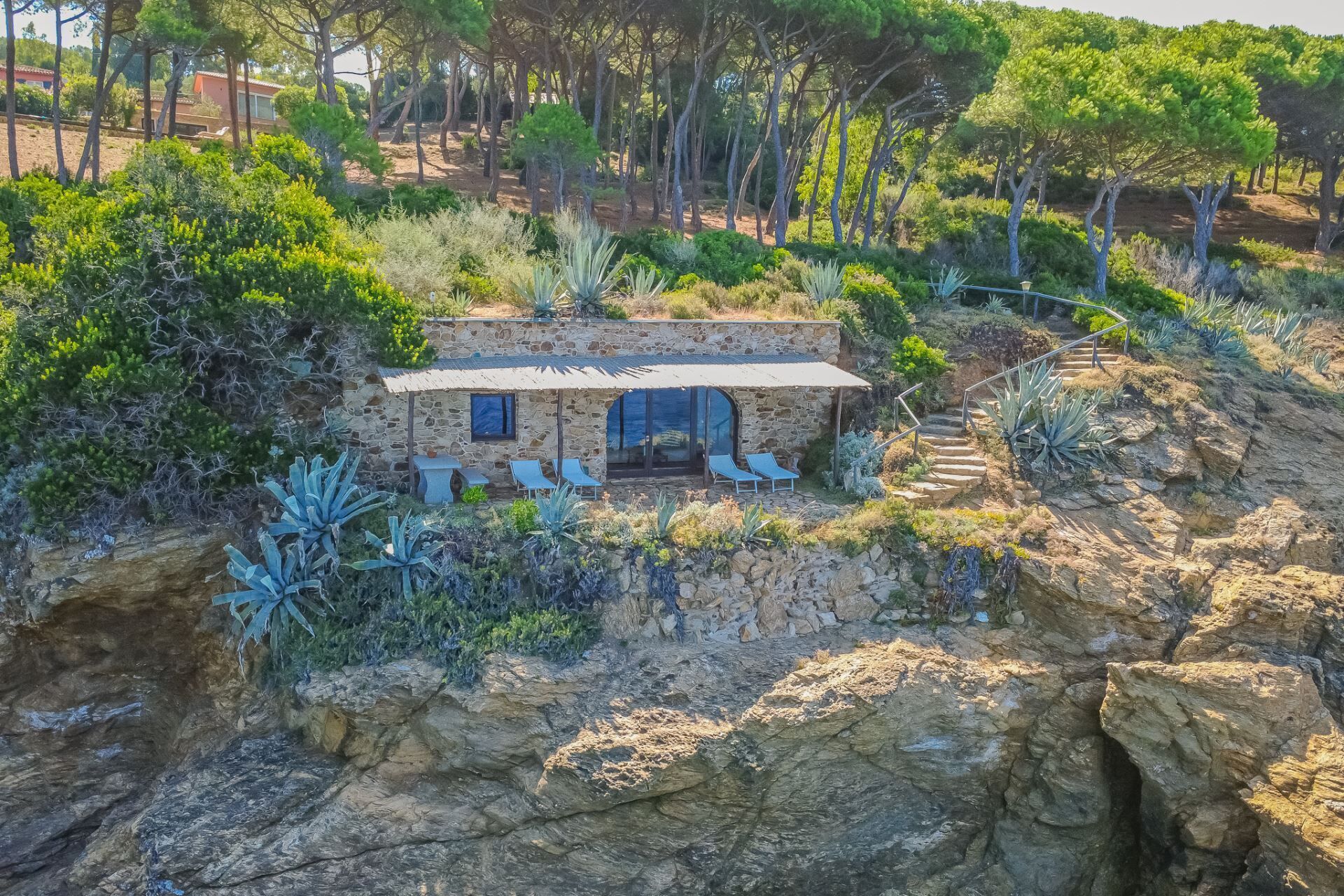 A stone house with a patio, surrounded by rocky terrain and vegetation.