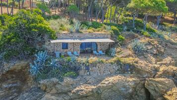 A stone house with a patio, surrounded by rocky terrain and vegetation.