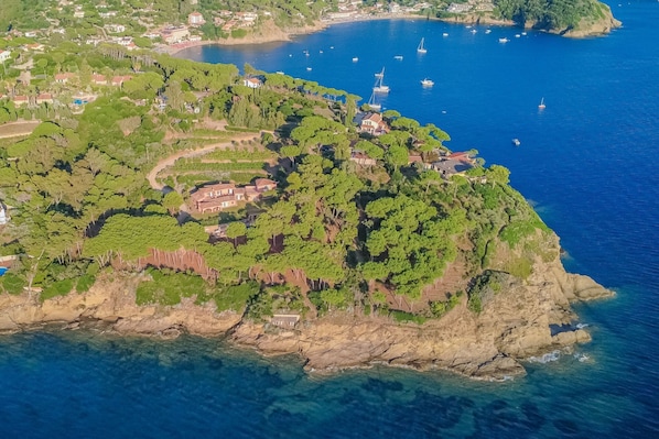 An aerial view of a coastal area with a cluster of buildings surrounded by greenery and rocky terrain.