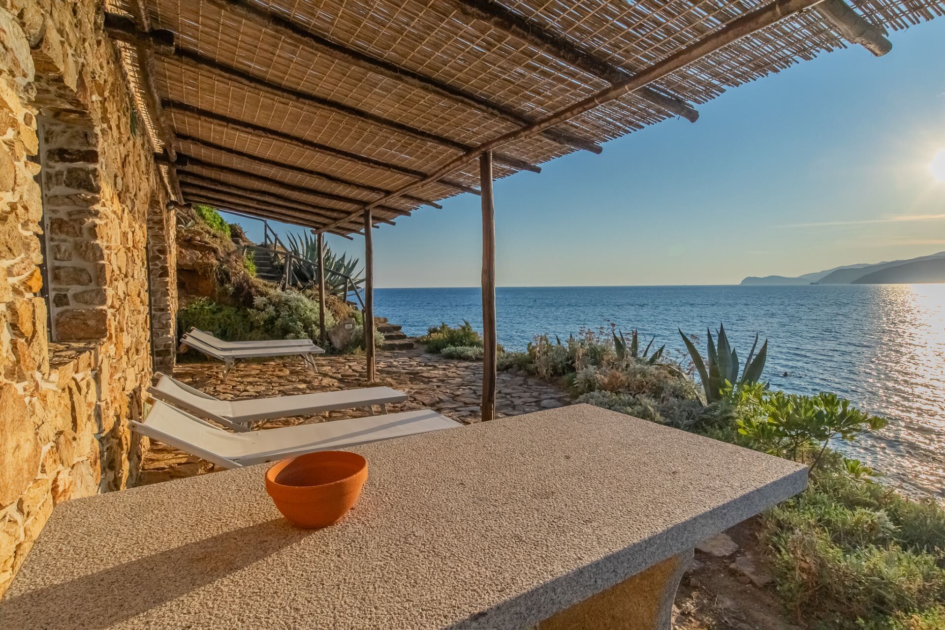 Un bâtiment en pierre avec un toit de chaume, un banc en pierre et une vue sur la mer.