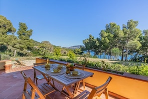 An outdoor dining area with a table set for four, surrounded by wooden chairs, overlooking a scenic landscape with trees and a body of water.