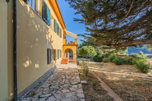 A building with a stone pathway leading to an archway, surrounded by greenery and trees. - Casale sul mare - Grilli 1 (Capoliveri)