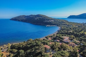 Une vue aérienne d’une zone côtière avec une plage, une petite île et un ensemble de bâtiments entourés de verdure.