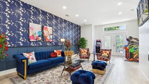 A modern living room with a blue sofa, a patterned rug, and a floral wall. - Spacious Dallas 4 bedroom Game Room & Spa 3 (Dallas)