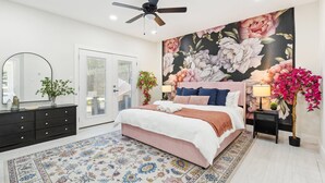A bedroom with a large bed, a ceiling fan, a floral wallpaper, a nightstand, and a potted plant. - Spacious Dallas 4 bedroom Game Room & Spa 3 (Dallas)