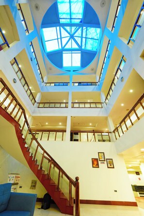 Un atrium à plusieurs niveaux, doté d’un escalier central, de grandes fenêtres et d’un plafond haut.