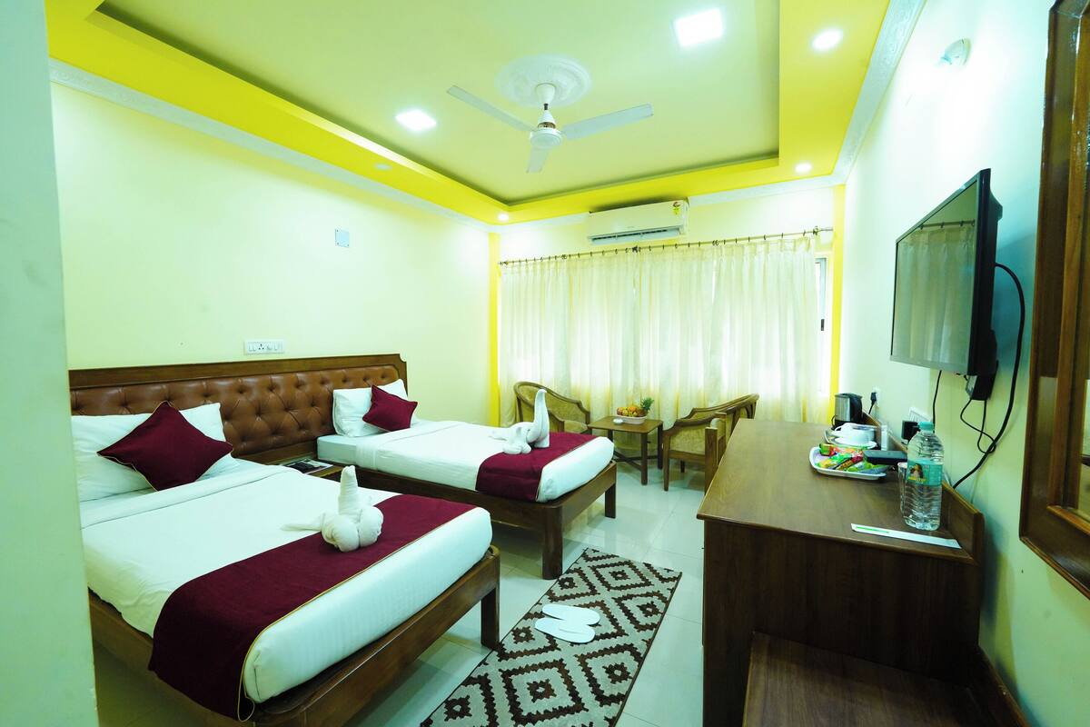 A hotel room with two beds, a desk, a chair, a television, and an air conditioning unit.