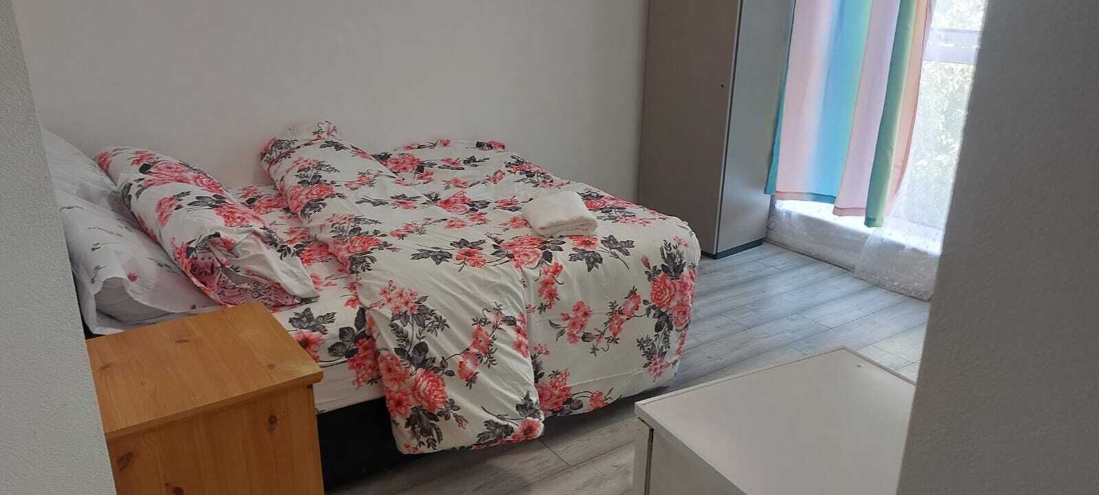 A bedroom with a bed, a wooden nightstand, and a window with curtains.