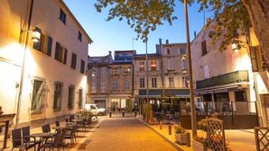 A cobblestone street with outdoor seating, buildings with multiple stories, and a tree providing shade. - L'Excellence, Love-room in Avignon (Avignon)