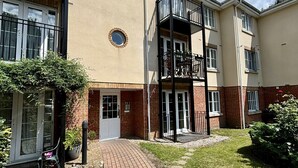 A multi-story residential building with a brick facade, a central courtyard with a brick pathway, and a small garden area. - Woking 2-Bed Flat with Balcony and Parking (Woking)