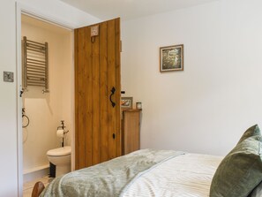 Un dormitorio con una cama, una puerta de madera, un inodoro y un pequeño armario.