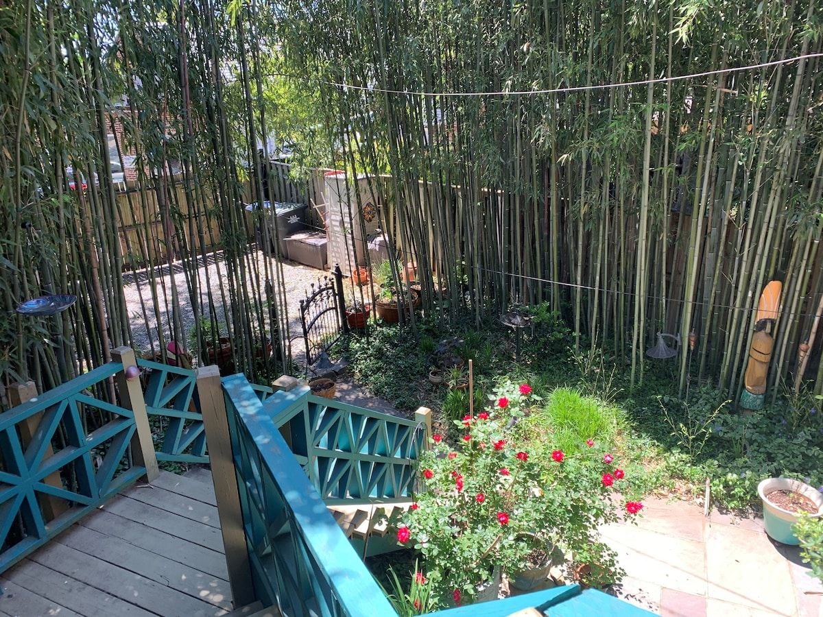 Un jardín con terraza de madera, valla de bambú y flores rojas.