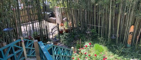 Un jardín con terraza de madera, valla de bambú y flores rojas.