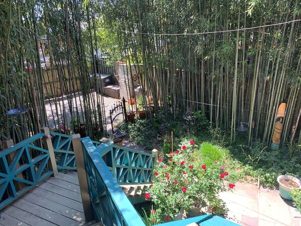 Un jardín con terraza de madera, valla de bambú y flores rojas.