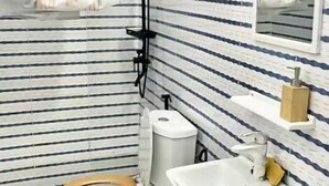 A bathroom with striped tiles, a toilet, a sink, and a shower. - Cosy studio at la riviera palmeraie (Abidjan)