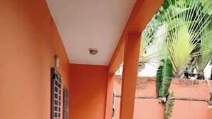 A corridor with orange walls and a tiled floor, leading to a covered outdoor area with a sandy ground. - Cosy studio at la riviera palmeraie (Abidjan)