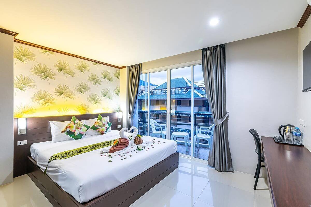 Quarto de hotel com cama, escrivaninha, cadeira e varanda com vista para prédios.