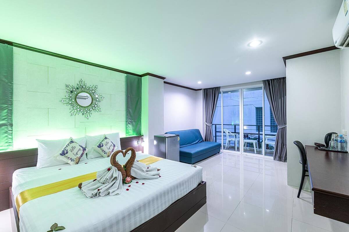 Quarto de hotel com cama, sofá azul, varanda com vista e escrivaninha com cadeira.