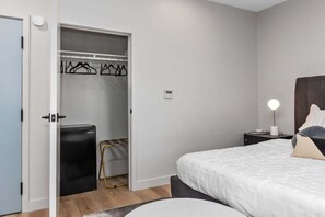 Ein Schlafzimmer mit einem Bett, einem Nachttisch, einer Lampe, einem Kleiderschrank und einem kleinen schwarzen Gerät.
