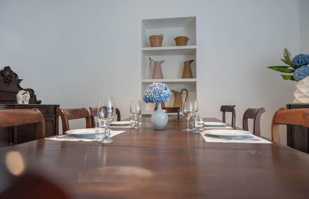 A dining table set with wine glasses and a vase of flowers, flanked by wooden chairs.