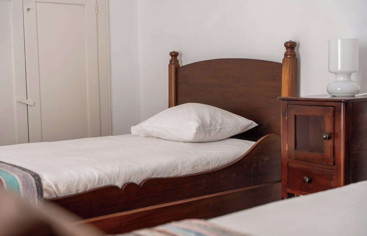 Una cama individual con cabecera de madera y una mesita de noche con lámpara.