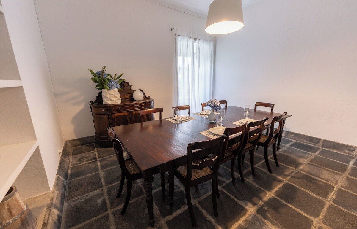 Un coin repas comprenant une table en bois, six chaises, un lustre et une fenêtre avec des rideaux.