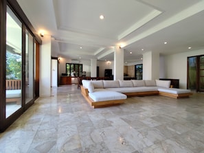 A spacious living area with a large sectional sofa, a wooden coffee table, and a marble floor.