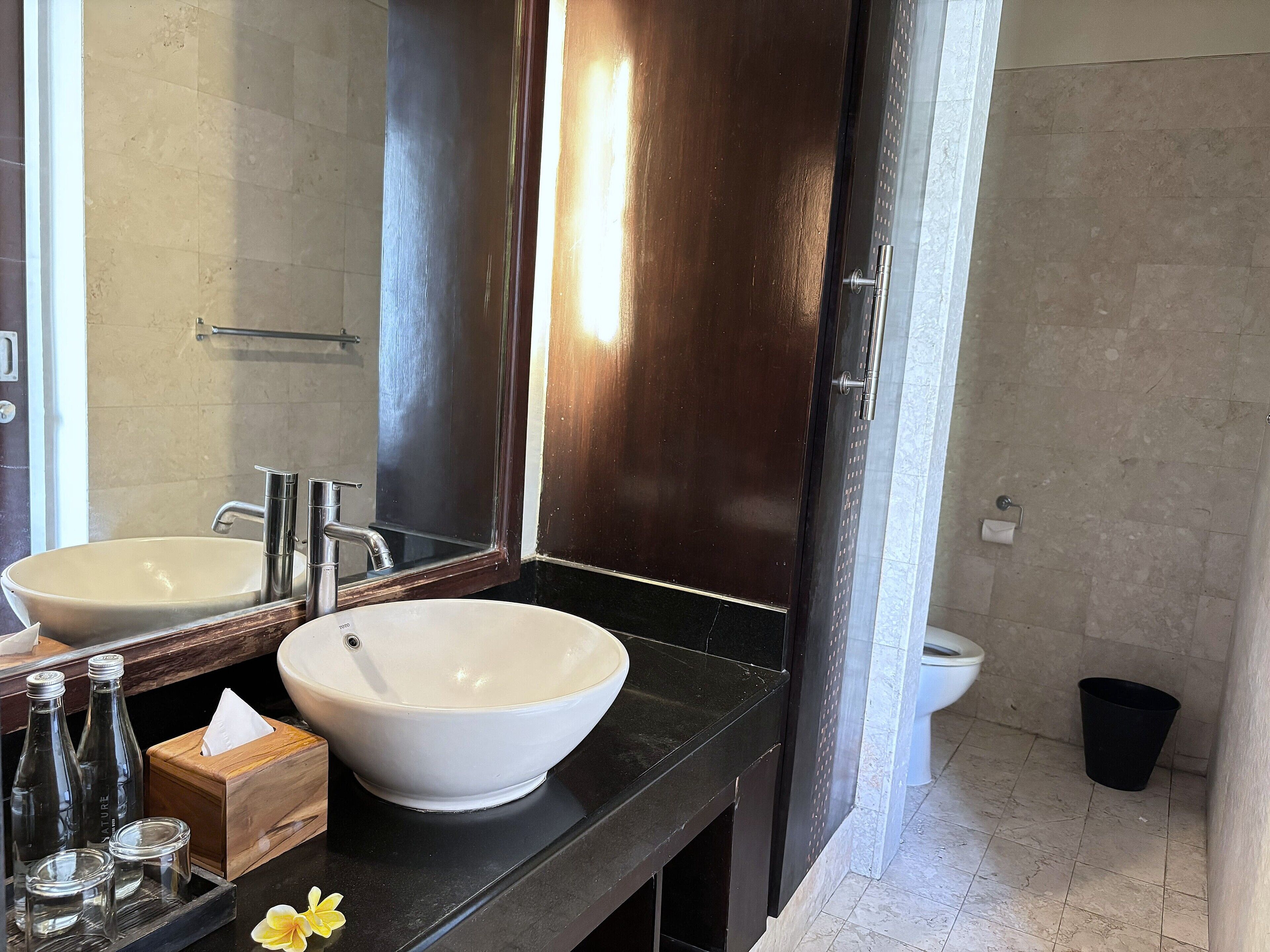 Une salle de bain avec deux lavabos, un miroir, un distributeur de serviettes et une poubelle.