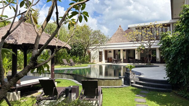A pool area with lounge chairs, a thatched-roof structure, and a building with a conical roof.