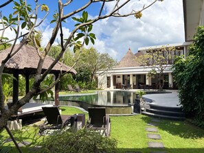 A pool area with lounge chairs, a thatched-roof structure, and a building with a conical roof. - 14 Bedroom Villa Riverside Legian (Legian)