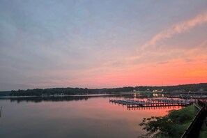 A calm lake with a dock and pier extending into the water, surrounded by trees and a distant shoreline.