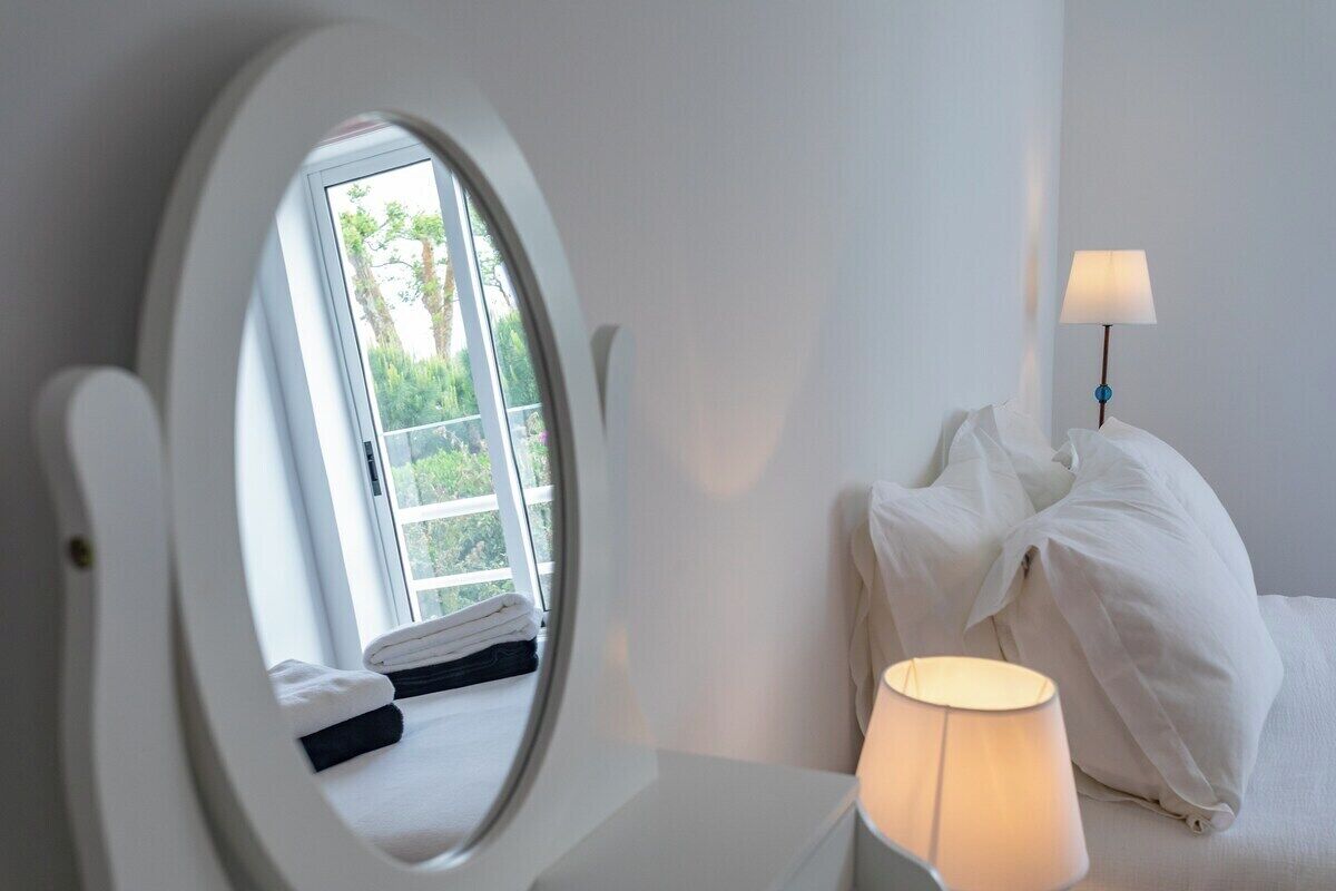 Ein Hotelzimmer mit Bett, Nachttischlampe, Fenster mit Blick auf Grünflächen und Spiegel.